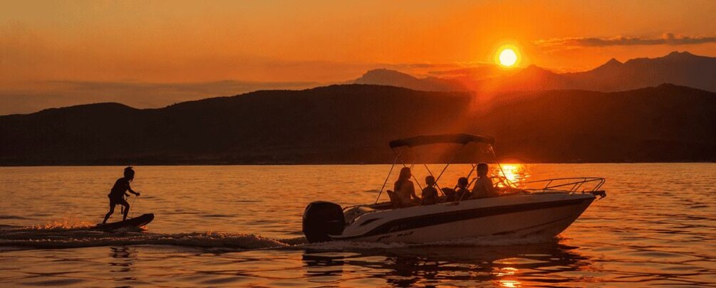 A sunset over a lake with a boat and a person wakeboarding. 1