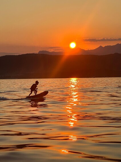 A sunset over a body of water with a silhouette of a person on a paddleboard. 4