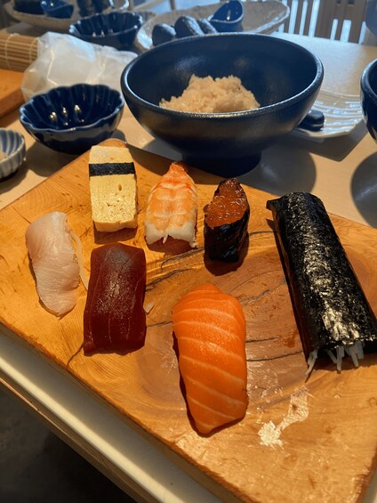A wooden board with various types of sushi, including salmon and tuna, and a bowl of rice in the background. 1
