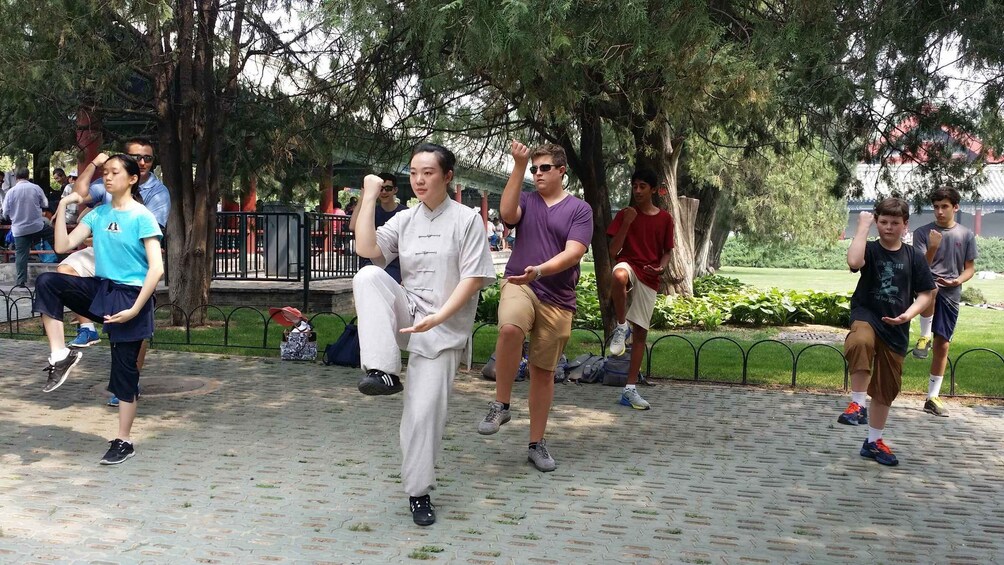 A group of people practicing martial arts in a park with trees and a paved walkway. 2