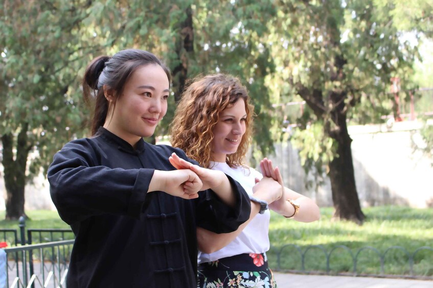 Two people demonstrating a martial arts move outdoors with trees and a fence in the background. 1