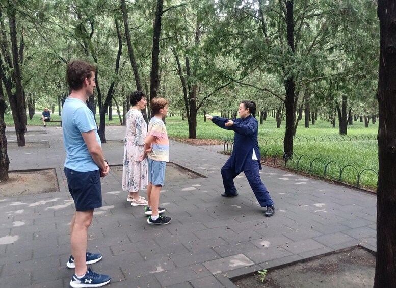 A person practicing Tai Chi in a park with trees and a paved path. 4