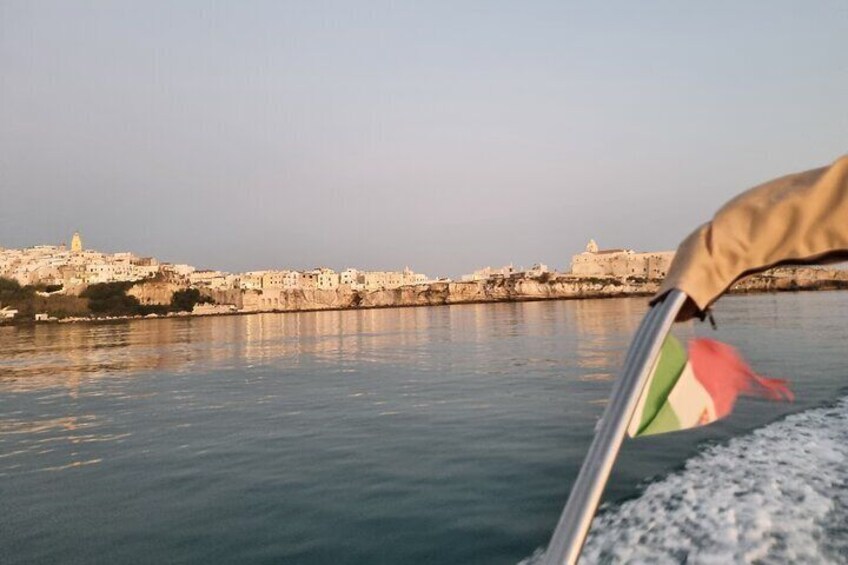 A coastal cityscape with a prominent hilltop fortress, calm waters, and a flag on a boat. 3