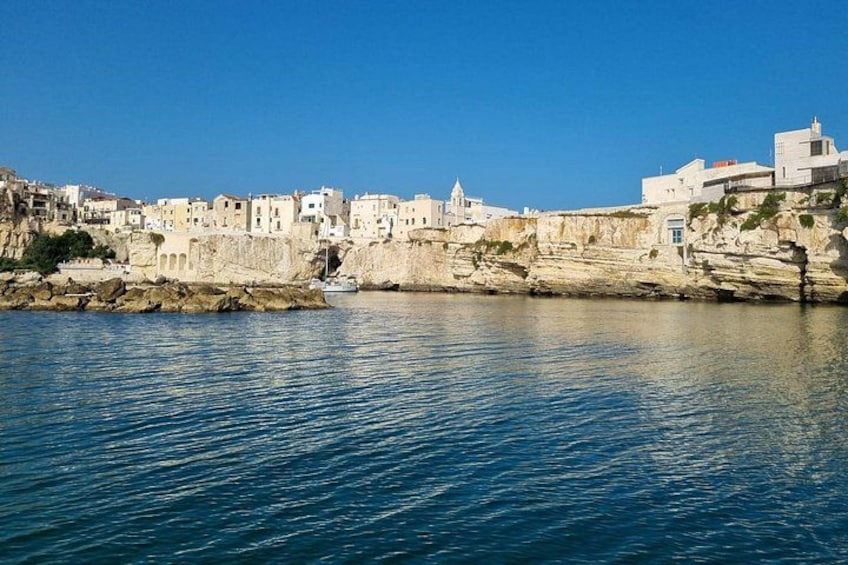 A coastal town with buildings on a cliff, calm sea, and clear sky. 1