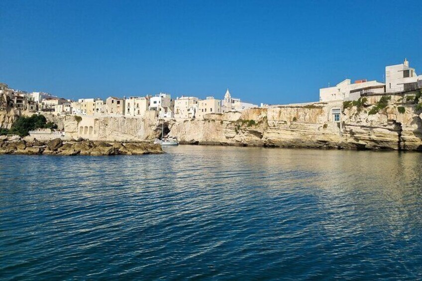 A coastal town with buildings on a cliff, calm sea, and clear sky. 1