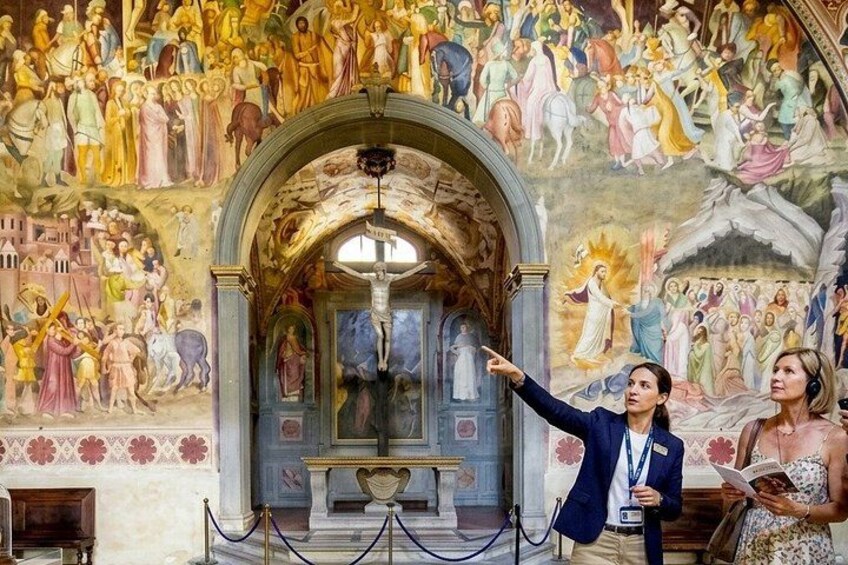 A church interior with a large fresco mural, a crucifix, and a robed figure pointing. 3