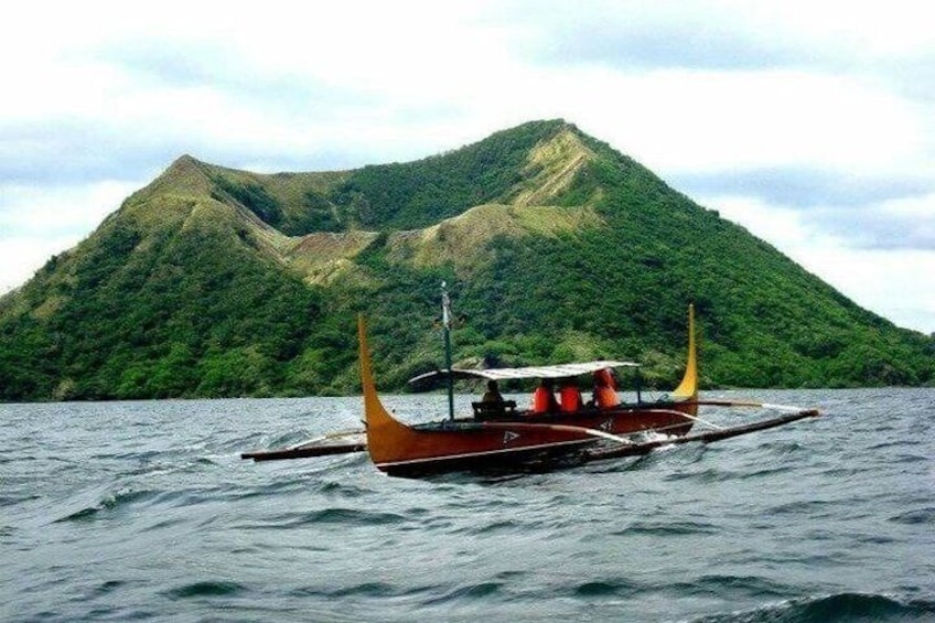 A traditional boat with a pointed bow and a single mast, sailing on calm waters with a green, mountainous island in the background. 3