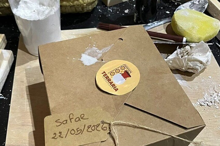 A brown paper bag with a sticker and a tag, placed on a wooden surface with various items around. 2