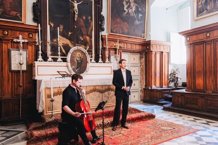 A man playing a cello in a church with a man standing beside him. 4