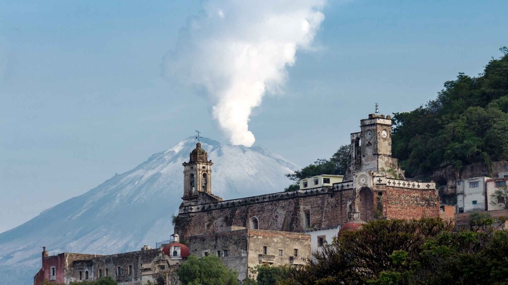 A historic building with two towers, a volcano in the background, and smoke rising from the volcano. 5