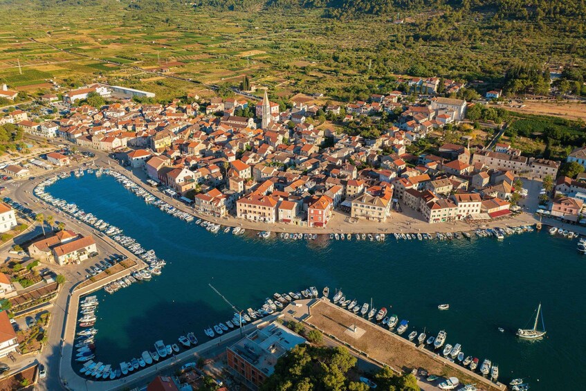 An aerial view of a coastal town with a marina, buildings, and surrounding greenery. 1