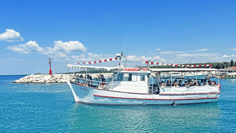 A white boat with red trim named 'GALEB' docked at a pier with a lighthouse in the background. 3
