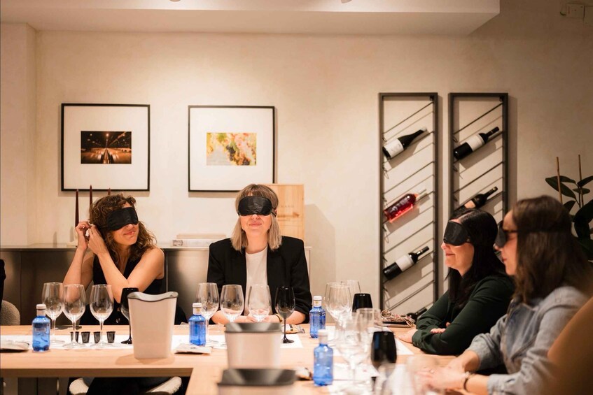 A group of people seated at a table with wine glasses and bottles, in a room with framed pictures on the wall. 1