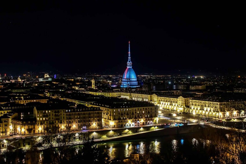 A nighttime cityscape with a prominent illuminated tower, a river reflecting lights, and historic buildings along the riverbank. 3