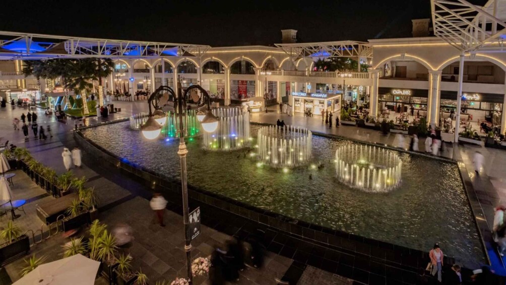 A nighttime shopping mall with a central water feature and illuminated arches. 4