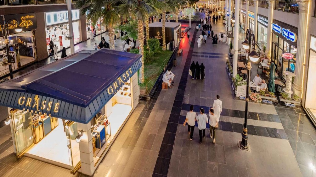 A shopping mall with a Grasse perfume store, palm trees, and people walking. 3