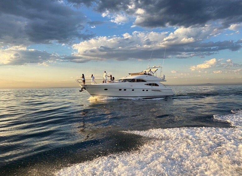 A white yacht with people on deck, sailing on calm waters under a partly cloudy sky. 1