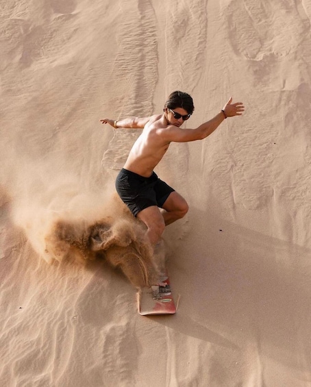 A person riding a sled on a sandy slope. 1