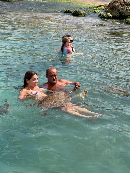 Three people swimming in clear water with rocks and greenery in the background. 4