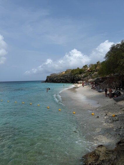 A beach with clear turquoise water, yellow buoys, and people relaxing on the sand. 1