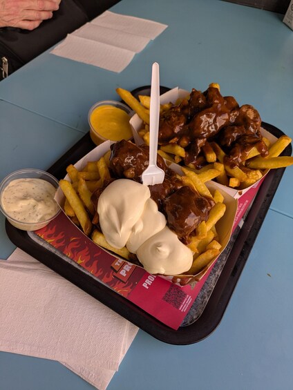 A tray with French fries, meatballs in gravy, and two types of dipping sauces. 3