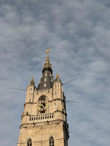 A historic tower with a clock, pointed spires, and a golden finial. 2