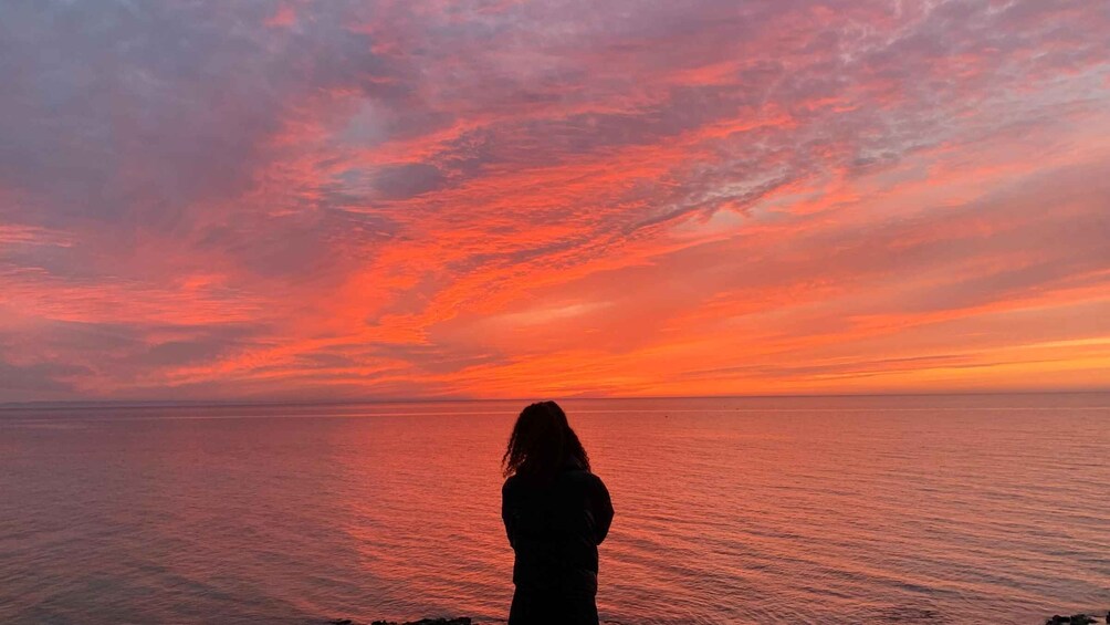 A silhouette of a person standing by the sea during a sunset with a vibrant sky. 1