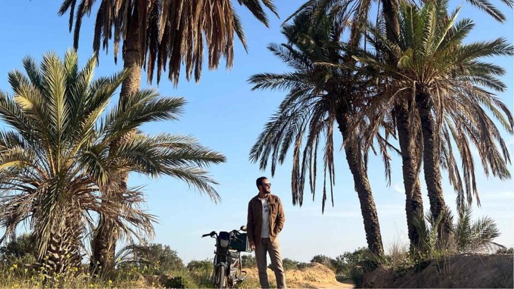 A person standing next to a motorcycle in a desert landscape with palm trees. 4