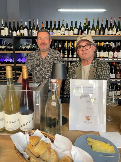 Two men at a wine tasting event with various bottles and a menu in front of them. 4