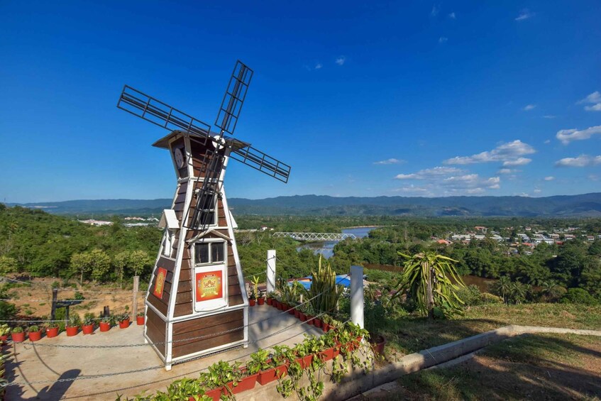Eine Windmühle mit einem Glockenturm, umgeben von viel Grün mit Blick auf eine Stadt und Berge. 1