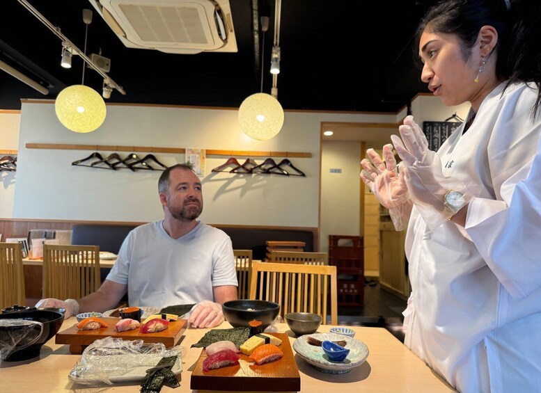 A sushi restaurant with a chef preparing sushi and a customer observing. 1