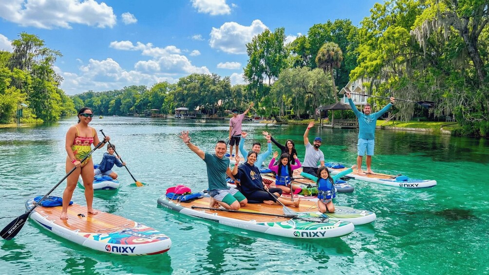 People paddleboarding on a river surrounded by trees and a house. 1