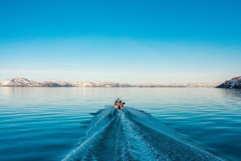 A boat moving through calm, turquoise water with snow-capped mountains in the background. 1