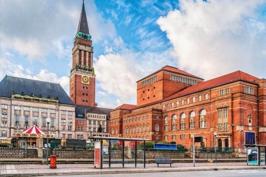 A historic building with a clock tower, a red brick structure, and a tram stop. 5