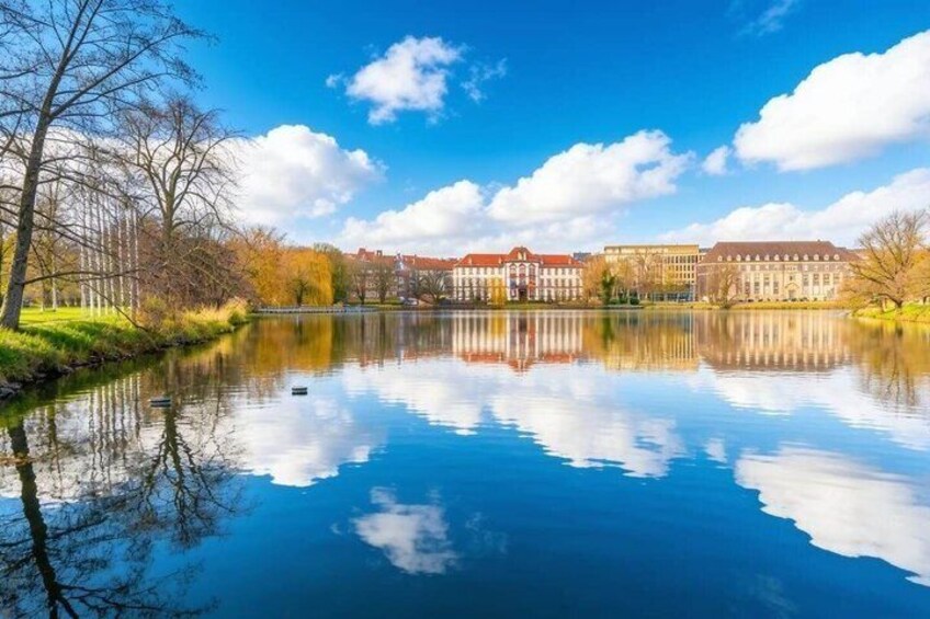 A calm lake reflecting buildings and trees under a clear sky. 4