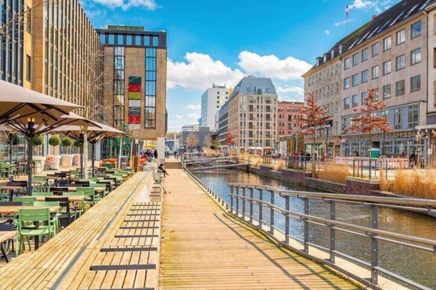 A riverside walkway with outdoor seating, a bridge, and buildings along the water. 3