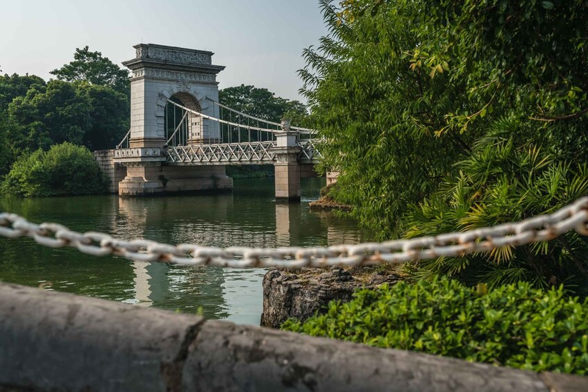 A suspension bridge over a river with a stone monument, surrounded by greenery. 2