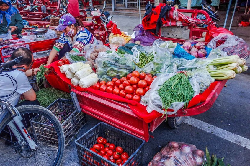 A street market with a red cart full of fresh produce like tomatoes, cucumbers, and onions. 5