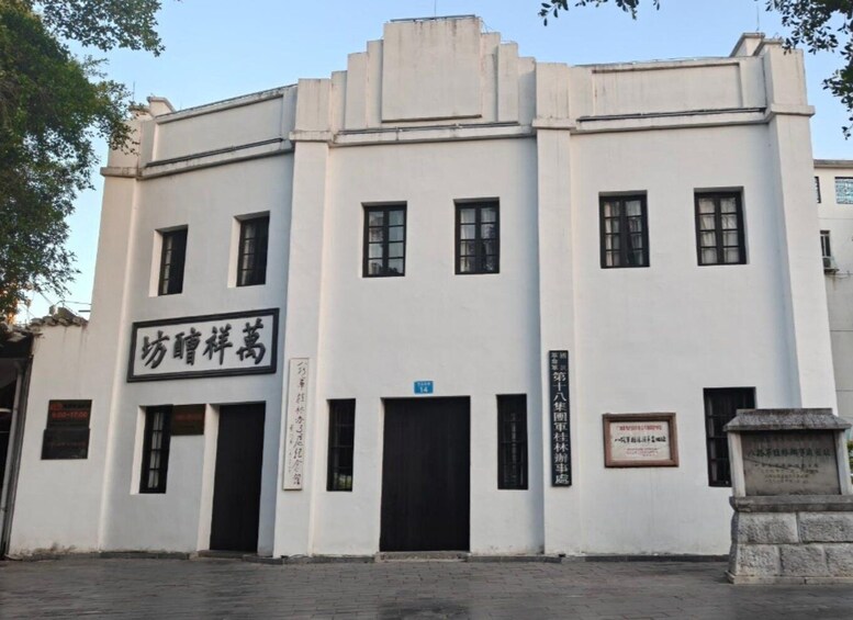 A white building with black-framed windows and doors, a sign with Chinese characters, and a stone monument in front. 3