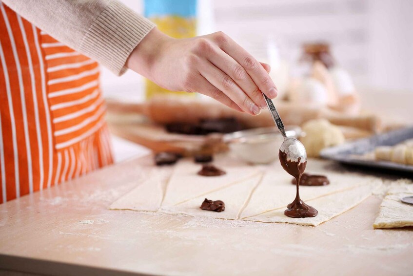 A person preparing food, specifically spreading chocolate on dough. 3