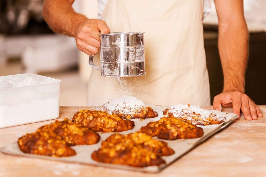 A person sprinkling flour on pastries. 1