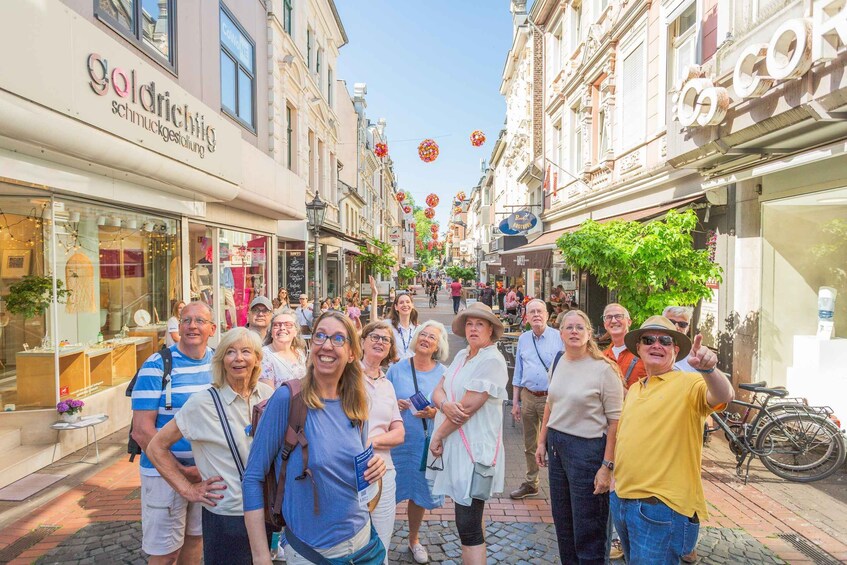A group of people standing on a cobblestone street lined with shops and buildings. 1