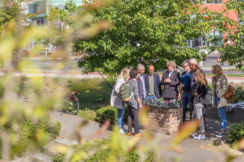 A group of people standing around a stone structure in an outdoor setting with trees and a building in the background. 3