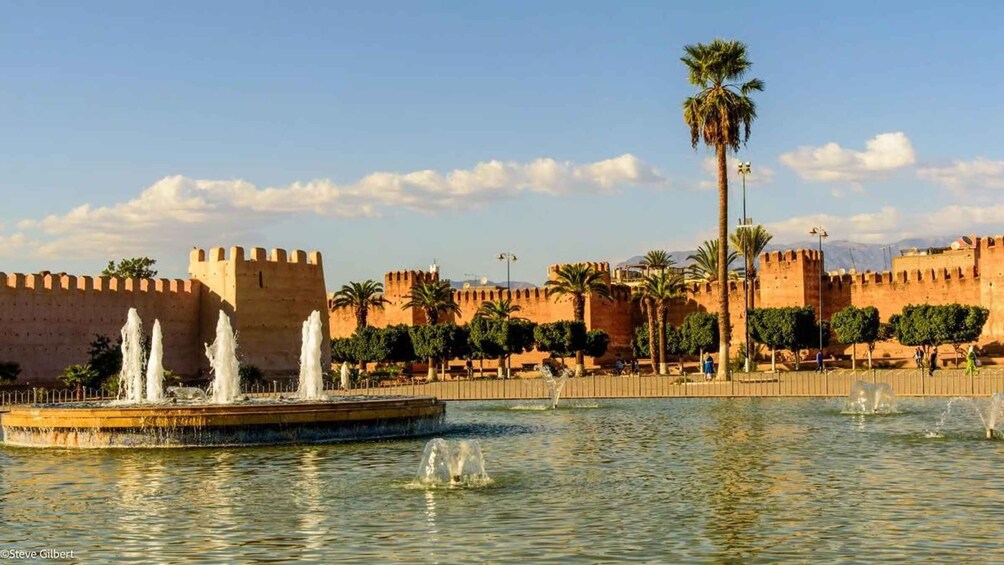 A historic fort with a moat and fountains, palm trees, and a clear sky. 1