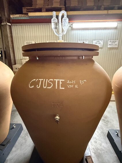 A large, brown, cylindrical tank with the inscription 'C'JUSTE 2025 75% VDF BL.' and a valve at the bottom. 3