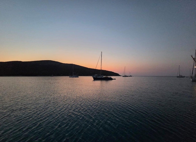 A calm sea at sunset with several sailboats anchored near the shore. 1
