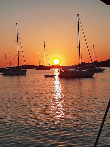A sunset over calm waters with sailboats anchored in the distance. 4