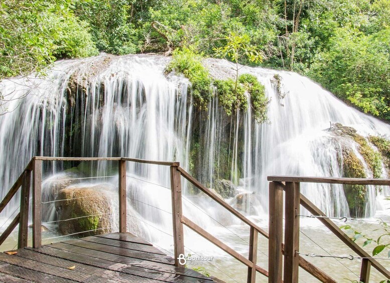 A wooden viewing platform overlooking a cascading waterfall surrounded by lush greenery. 1