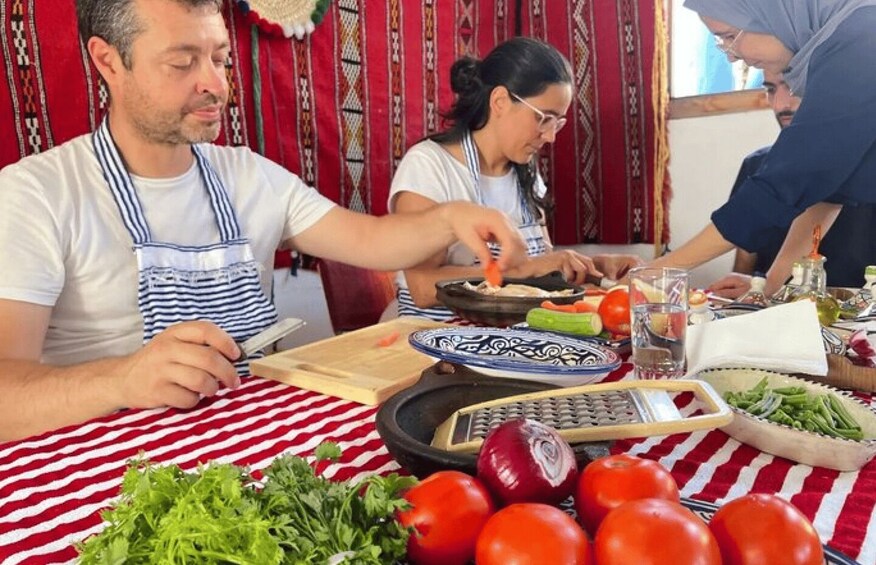 People preparing food at a table with vegetables and a cutting board. 1