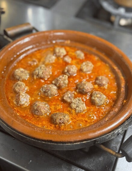 A clay pot with meatballs simmering in a tomato-based sauce. 3
